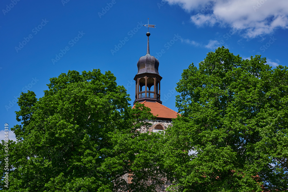 View to the tower of a medieval village church in the state of Brandenburg, Germany, that can be seen through trees.