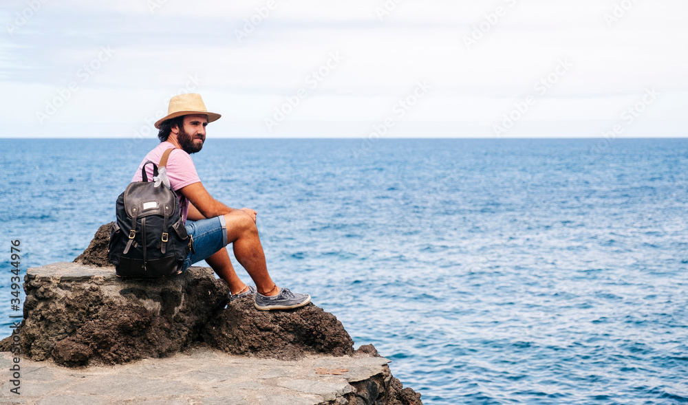 A tourist man with hat and backpack on a rock on the coast with the sea in the background. El Hierro, Canary Islands
