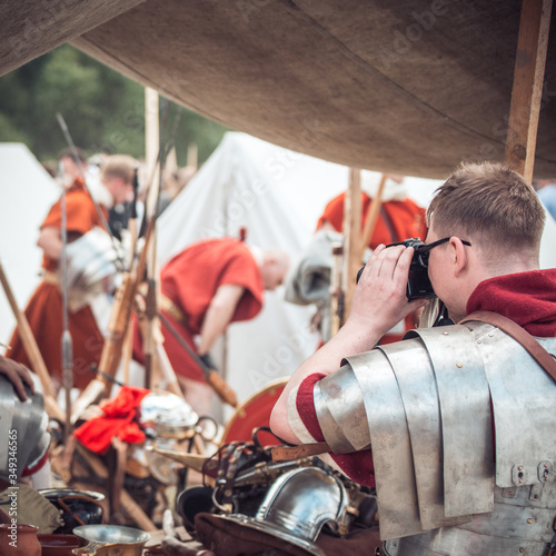A man in armor of a Roman legionnaire warrior photographs his friends at a festival of reenactors