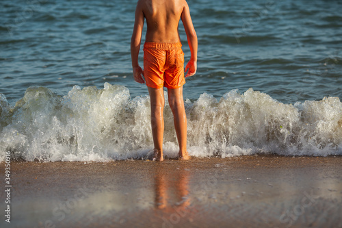 Un niño en la playa mirando al mar con olas rompiendo en la orilla verano