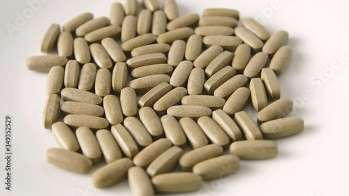 Herbal medicine tablets (black walnut leaves) fall onto a white plate and scatter. Concept for self-medication, natural medicine and dangers of overdose
