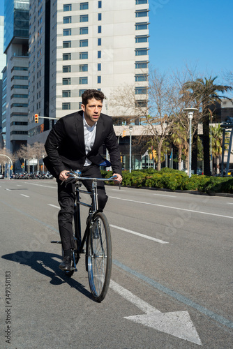 Fototapeta Naklejka Na Ścianę i Meble -  Citizen dressed in suit rides a bicycle along a city street- vertical