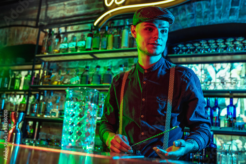 Professional barman proposing alcoholic cocktails, shots, beverages to guest in multicolored neon light. Entertainment, drinks, service concept. Modern bar, crafted beverages, trendy neoned colors.