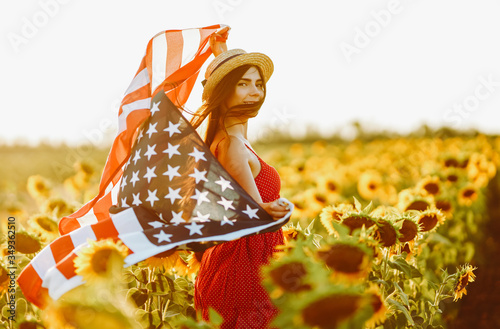 4th of July. Amazing girl in hat with the American flag in a sunflower field. Freedom day. Sunset light. Independence Day. Patriotic concept 