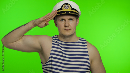 Young sailor man salutes with hand to camera. Seaman guy in sailor's vest