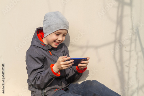 A person is playing a game on their blue smartphone. A teenager smiles and laughs in the street.