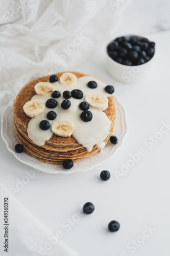 Pancakes with condensed milk with fresh blueberries and banana in a white plate on a white background.