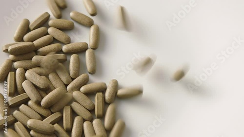 Herbal medicine tablets (black walnut leaves) fall onto a white plate and scatter. Concept for self-medication, natural medicine and dangers of overdose. Copyspace on the side