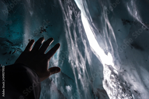 Hand reaching the ice inside a cave in Matanuska Glacier, Alaska. Looks like a person trapped, in distress, asking for help; confined, caught, imprisoned; all while walking, trekking on the snow.