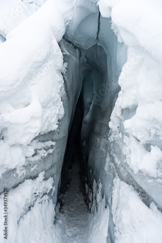 Entrance of an ice cave in Matanuska Glacier, Alaska; covered with snow. Details of the surface; texture. Taken during a trek in winter holidays. Dark interior. Endless gloomy tunnel. White. photo