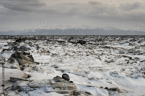 Frozen beach with its ice breaking and melting on the coast of Anchorage, Alaska. Beautiful landscape showing global warming and climate change. No sand, just snow, ice and rocks. Snowy mountains.