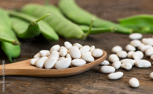 Uncooked dried white haricot beans in wooden spoon with fresh raw green beans pod plant on rustic table. Heap of legume haricot bean background ( Phaseolus vulgaris )