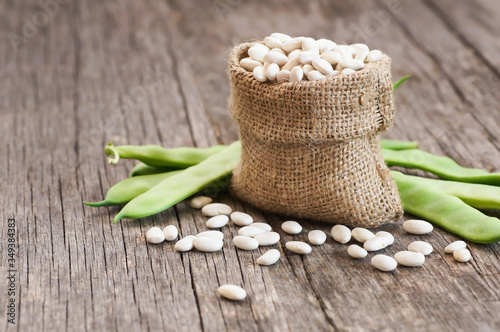 Uncooked dried white haricot beans in burlap sack with fresh raw green beans pod plant on rustic table. Heap of legume haricot bean background ( Phaseolus vulgaris )