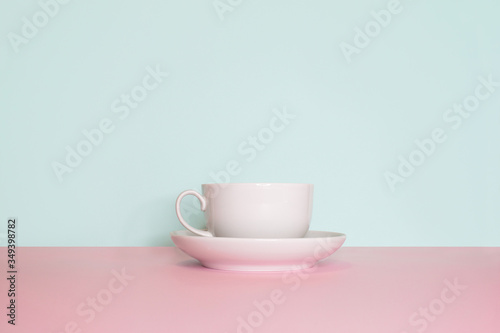 Side view on a still life. White cup with saucer on a bright pink and mint background. 