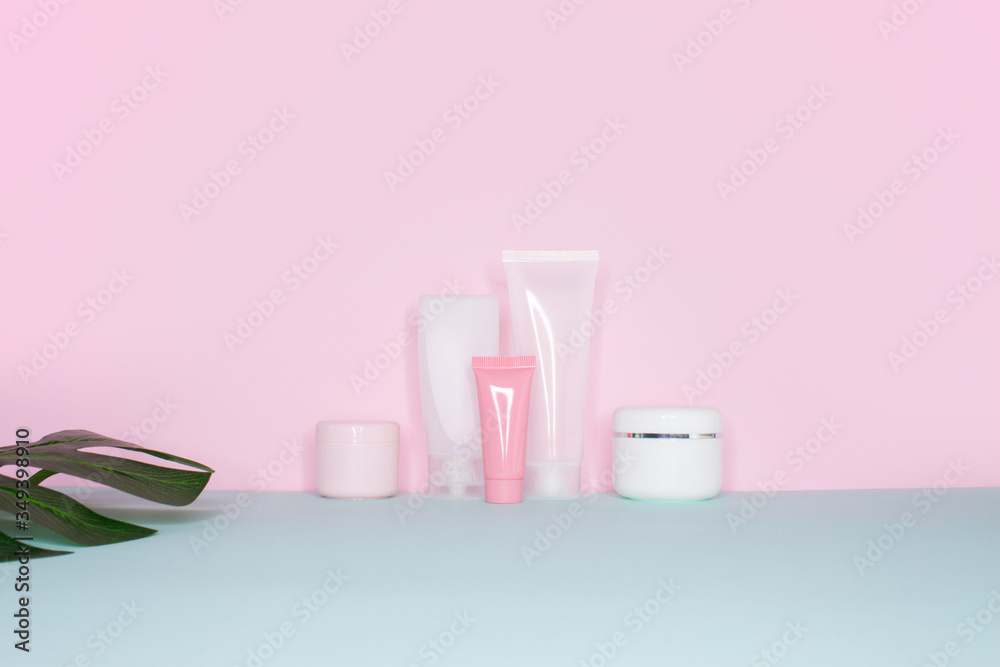 Side view on a still life. Group of empty cosmetic bottles and green monstera leaf on a bright pink and mint background. 