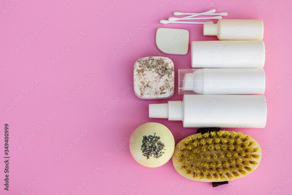 White cosmetic bottles, bath bomb, handmade soap, bath salt, massage brush, sponge, cotton buds with cherry flowers on a pink background. Natural organic cosmetics concept. White cosmetic bottles, bath bomb, handmade soap, bath salt, massage brush, sponge, cotton buds with cherry flowers on a pink background. Natural organic cosmetics concept.