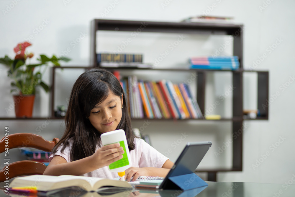 Mexican little girl pasting homework cutout, doing homework online at home due to quarantine, homeschool Mexican little girl pasting homework cutout, doing homework online at home due to quarantine, homeschool