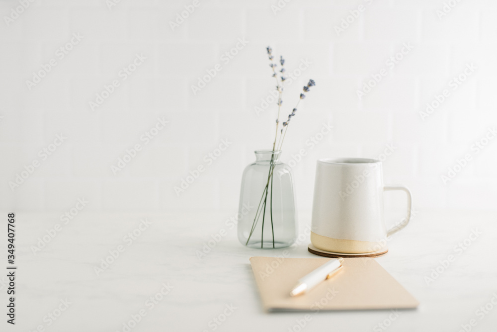 Straight on view of clean, minimal desk with coffee mug, notebook and glass vase