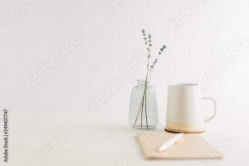 Straight on view of clean, minimal desk with coffee mug, notebook and glass vase