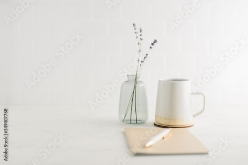 Straight on view of clean, minimal desk with coffee mug, notebook and glass vase