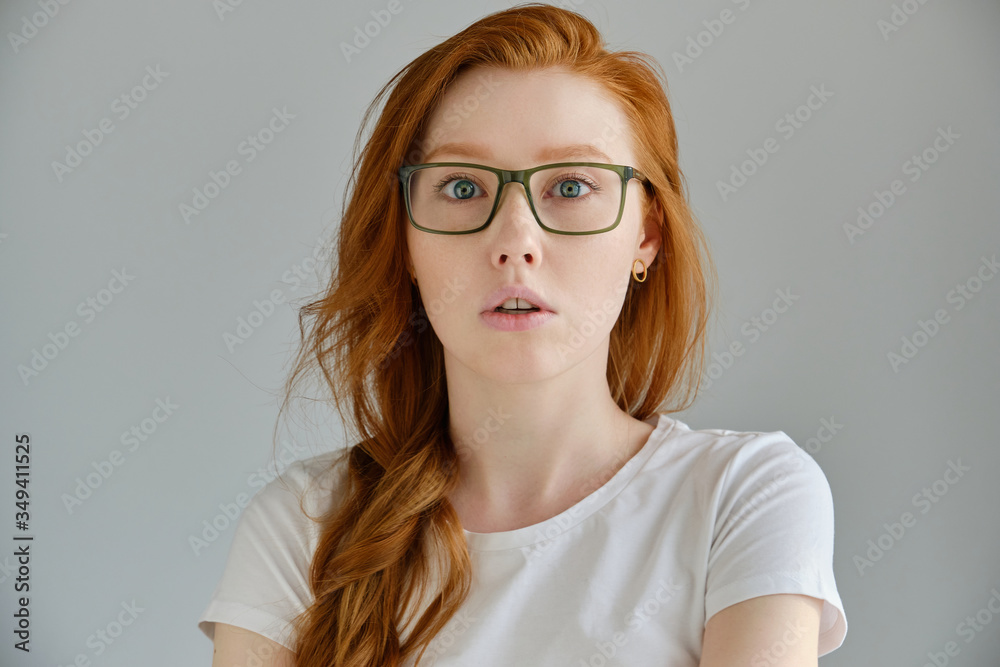 A red-haired girl in a white T-shirt and glasses looks surprised at the opening of mouth in the frame A red-haired girl in a white T-shirt and glasses looks surprised at the opening of mouth in the frame