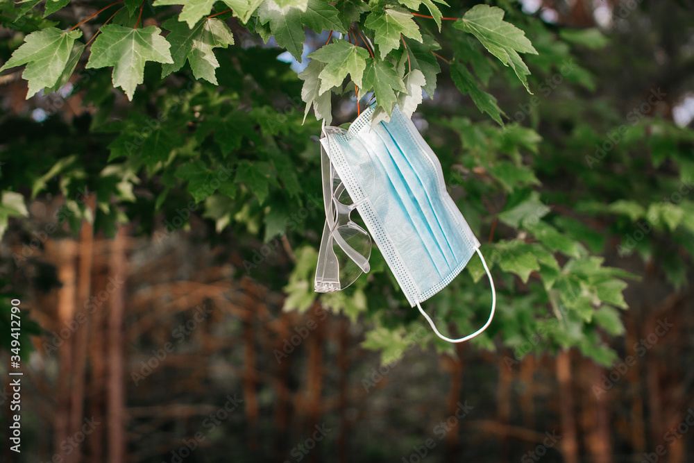 Surgical mask and glasses hang on branch with green leaves in sunset. Healthcare. Coronavirus protection