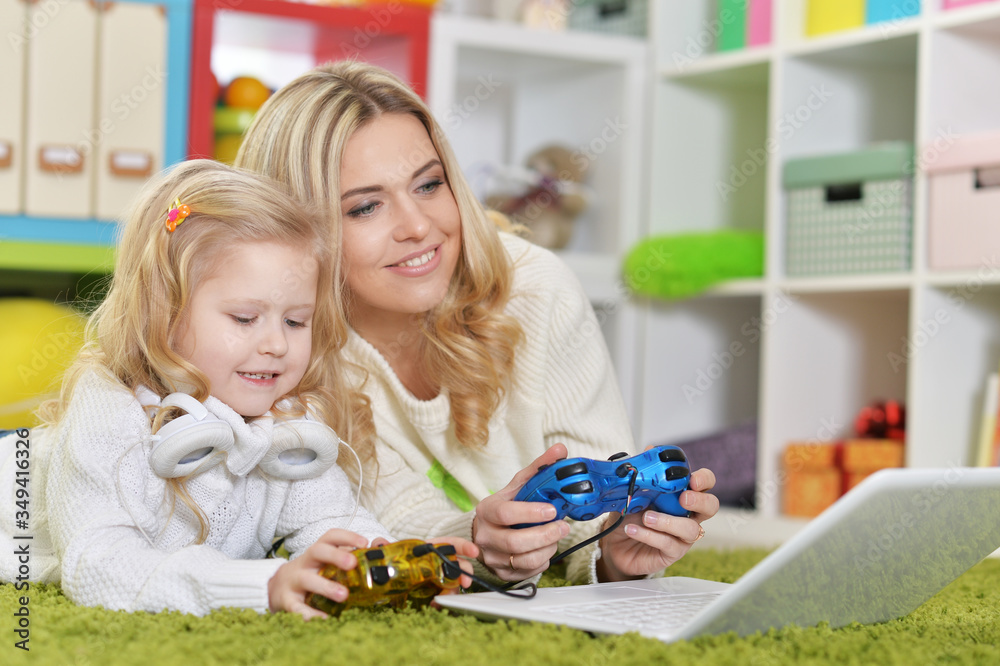 Mother with little daughter playing computer games with laptop