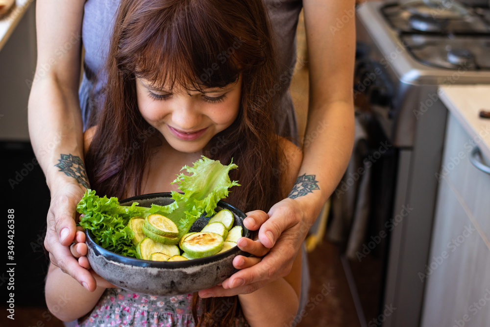 Mother and girl hold vegan food in hands together - baked zucchini. Family care and healthy meal concept. Mother and girl hold vegan food in hands together - baked zucchini. Family care and healthy meal concept.