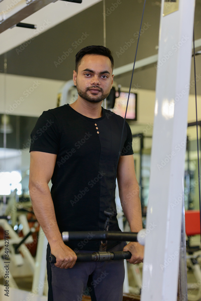 Young bearded Indian man using exercise equipment at the gym