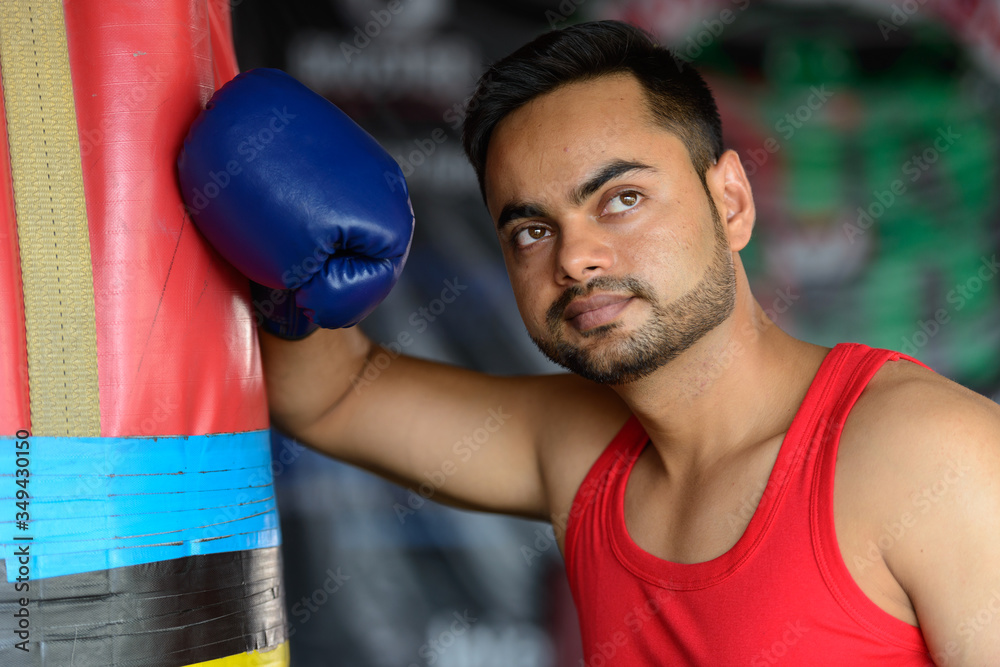 Face of young handsome bearded Indian man as boxer thinking at the gym