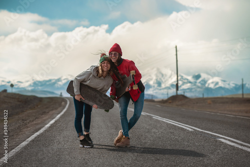 Fototapeta Naklejka Na Ścianę i Meble -  Two happy girls with longboards at mountain road