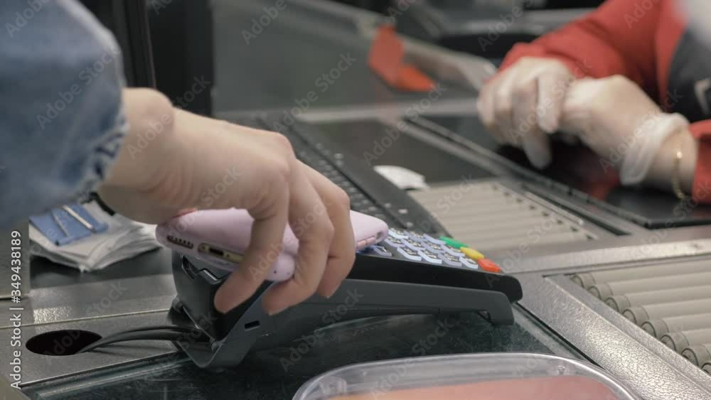At the supermarket: checkout counter customer pays with smartphone for her food items. Big shopping mall. Small lines and modern wireless paying terminal system. At the supermarket: checkout counter customer pays with smartphone for her food items. Big shopping mall. Small lines and modern wireless paying terminal system.