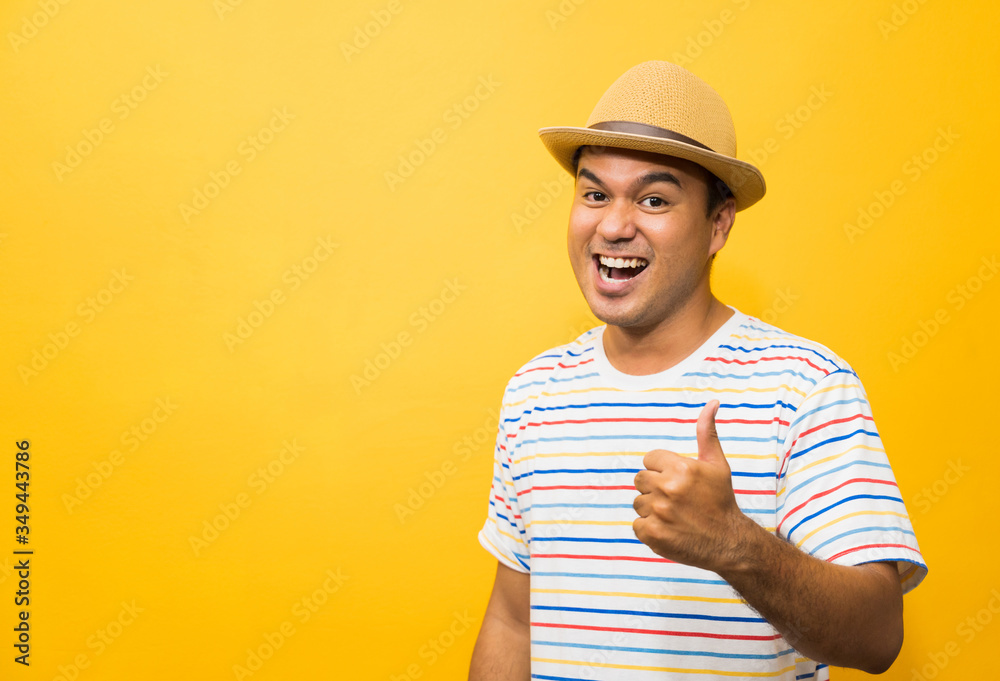 Young Asian man with hat feels happy  and surprise and showing thumb up on yellow background.