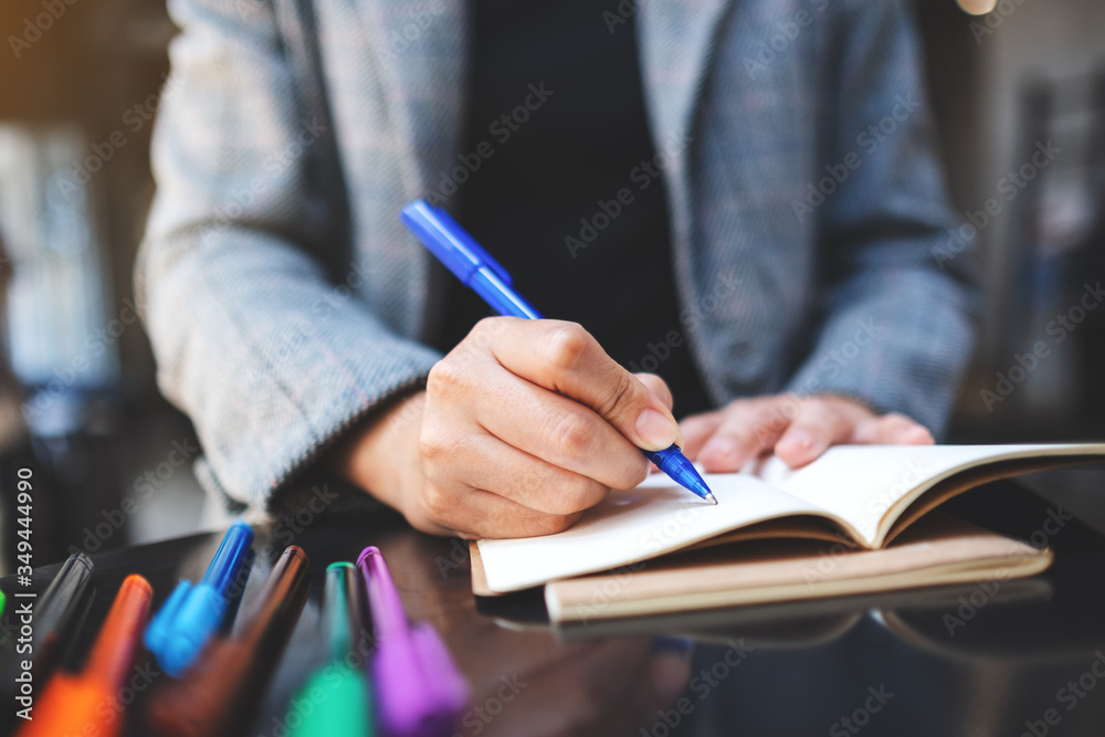 Closeup image of a woman writing on a blank notebook with colored pens on the table Closeup image of a woman writing on a blank notebook with colored pens on the table