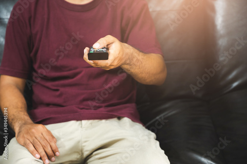 Young man holding television remote control. Hands pointing to tv set and turning it on or off select channel watching tv on his sofa at home in the living room relax..