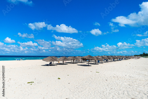 A lot of straw umbrellas standing in a row and sun loungers stand on the white sand against a blue cloudy sky. Varadero, Matanzas Province, Cuba photo