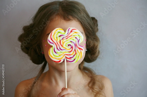 A girl holds a colorful Lollipop on a stick in front of her face.