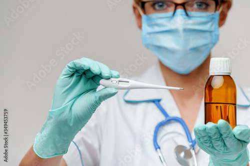 medical doctor nurse woman wearing protective mask and rubber or latex gloves - holding can of medicine and thermometer