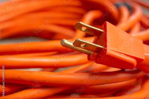 A closeup view of a male end plug of a coiled orange extension cord.