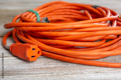 A view of an orange extension cord, featuring the female plug end, seen on a wooden surface. photo
