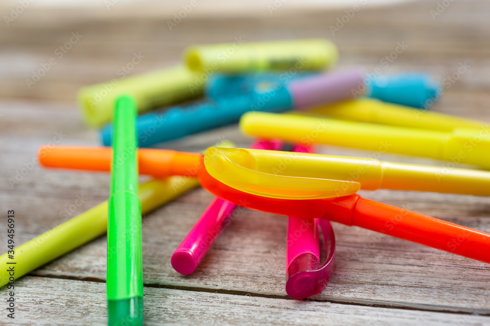 A closeup view of a pile of colorful highlighters on a wooden surface.