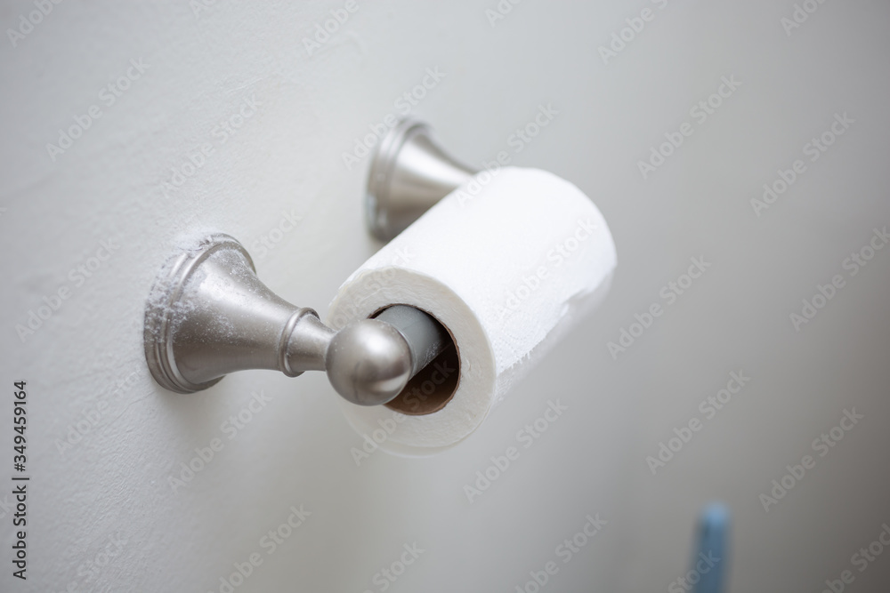 A view of a half used roll of toilet paper on a wall dispenser, in a bathroom setting. A view of a half used roll of toilet paper on a wall dispenser, in a bathroom setting.