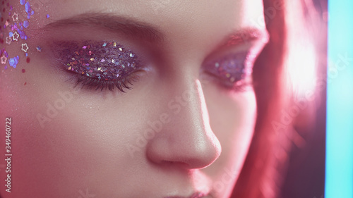 Glitter eyes. Creative fashion makeup. Woman face with sparkles on skin in pink neon light.