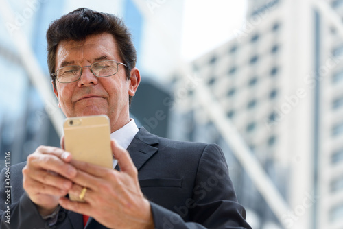 Mature businessman using mobile phone in front of modern building at Bangkok city