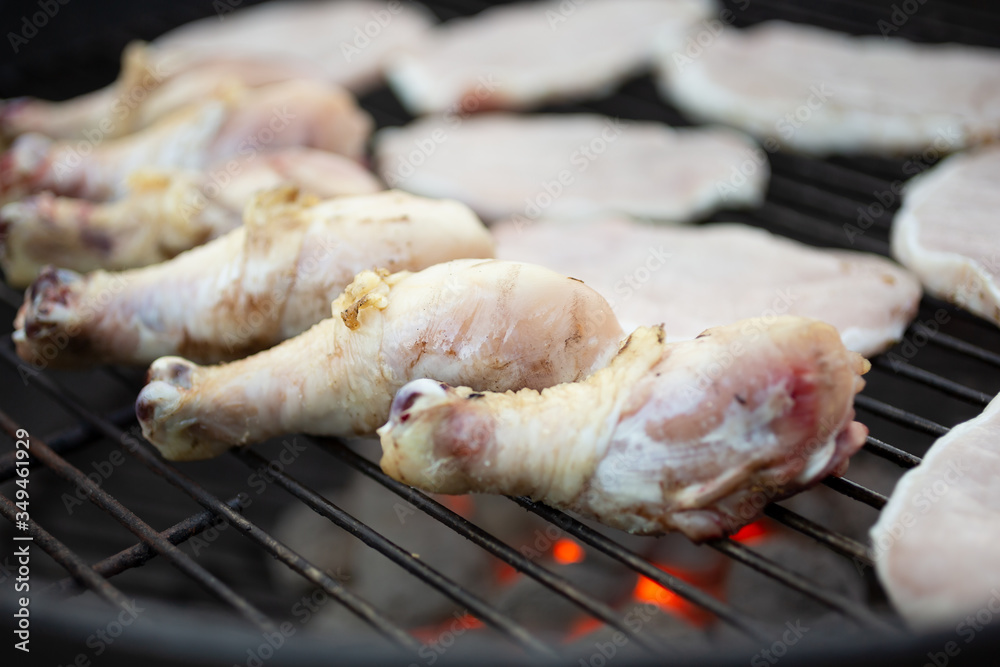 A closeup view of several raw chicken drumsticks on a grill. Glowing briquettes are underneath.