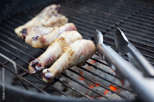 A closeup view of raw chicken drumsticks cooking on a charcoal barbecue grill.
