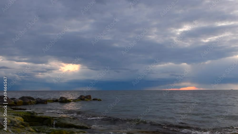 sunset storm clouds over ocean with boulders in foreground