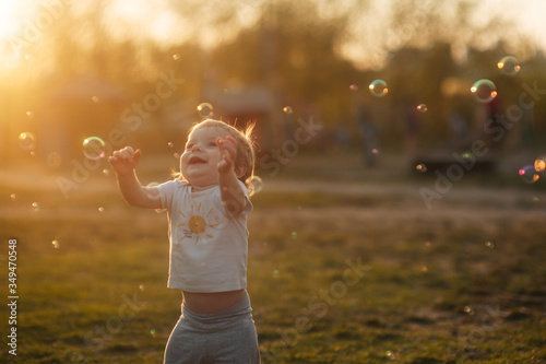 little smiling boy plays with soap bubbles in a clearing at sunset at golden hour