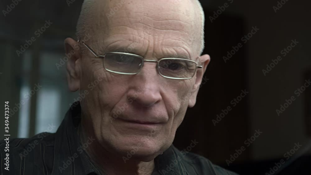 elderly bald man with wrinkles on face wearing glasses sews with hands in dark room at home extreme close view