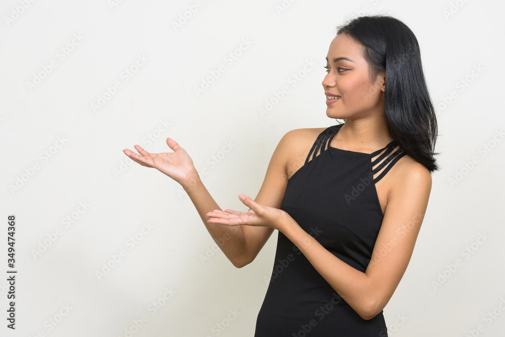 Profile view of happy young beautiful Asian businesswoman showing something Profile view of happy young beautiful Asian businesswoman showing something